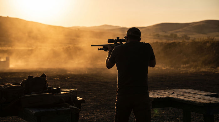 Shooter sighting a scoped rifle at golden hour